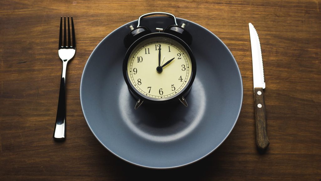 A clock on a plate with a knife and fork on the side to indicate fasting